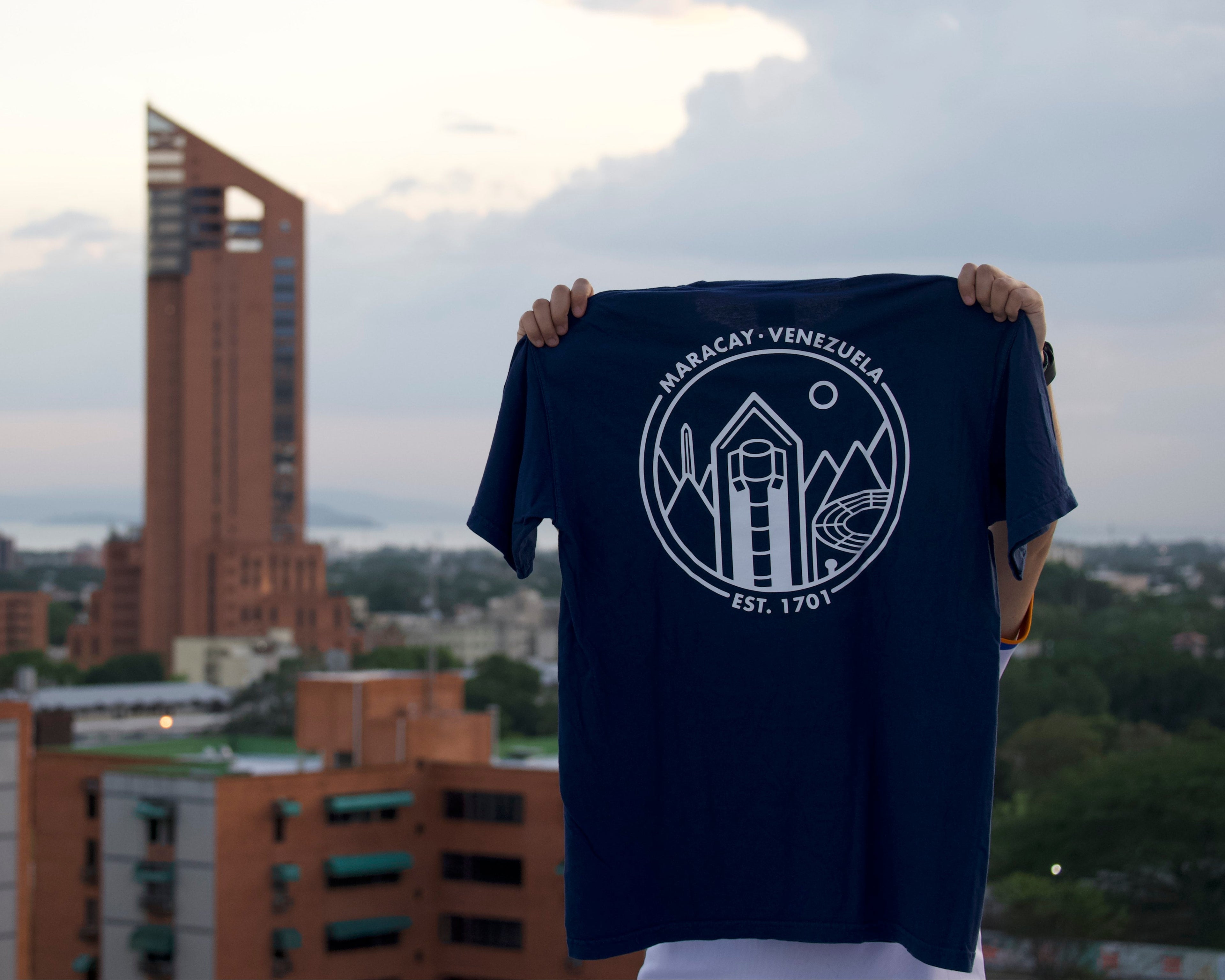 Person holding a t-shirt with a logo against an urban skyline